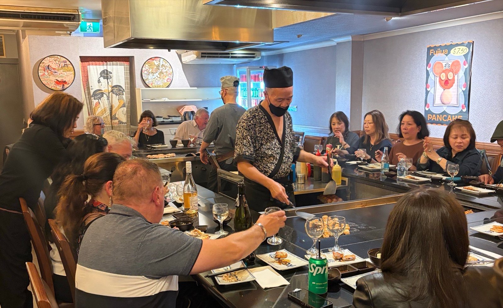 A full house at Fujiya: guests seated shoulder to shoulder around both teppanyaki hotplates while the chef cooks in the middle