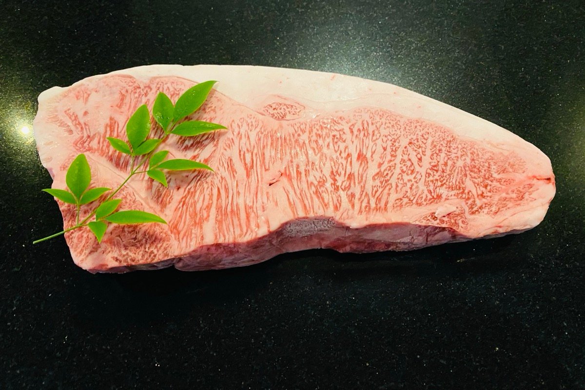 Raw Japanese A5 wagyu, its fat marbled through the meat like fine lace, on black granite with a sprig of green leaves