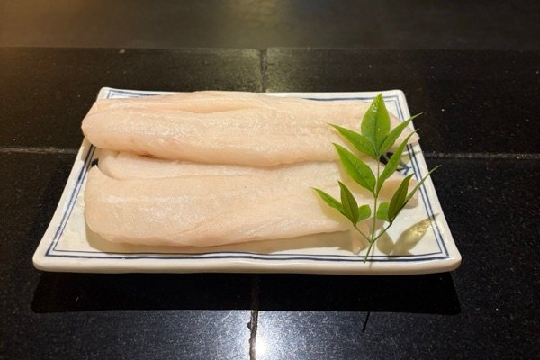 Raw deep sea perch fish fillets on a blue and white plate with a sprig of green leaves, on the black granite counter